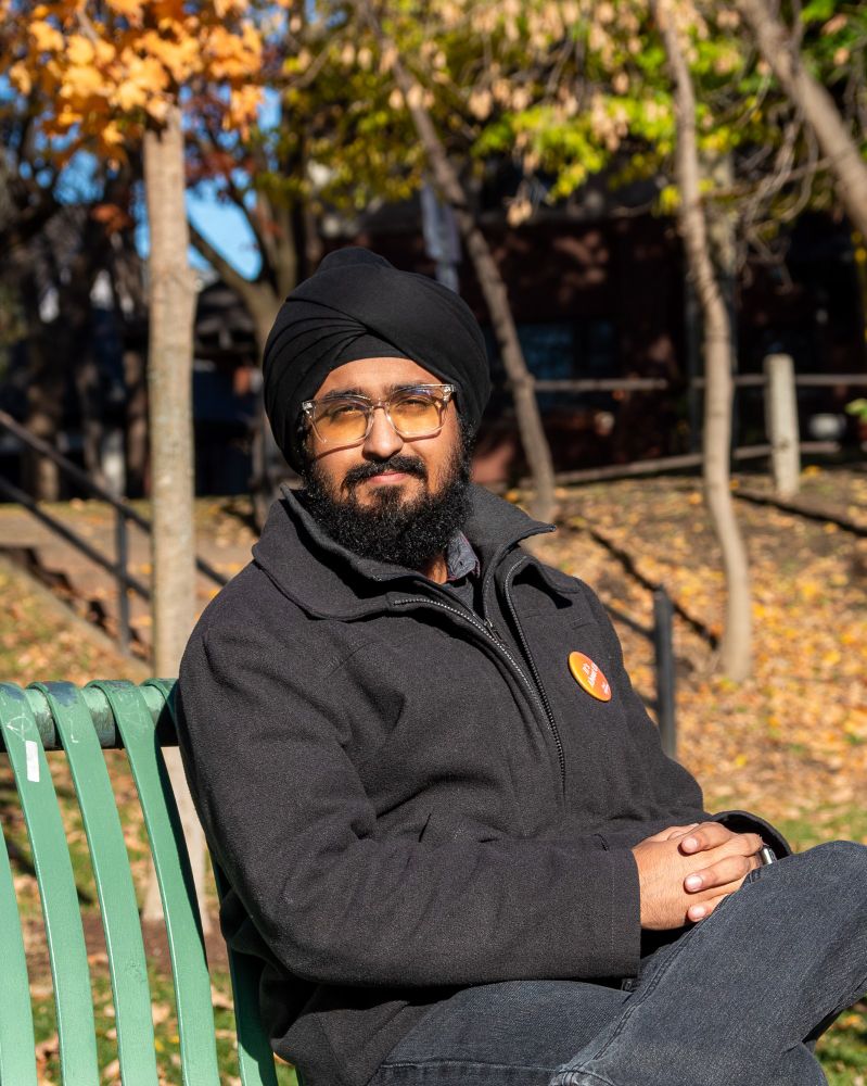 Jay sits on a park bench in a park on a fall day