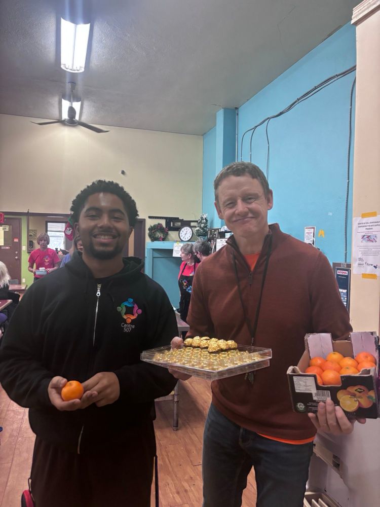 Joel with a volunteer at Centre 507, holding oranges and chocolate 