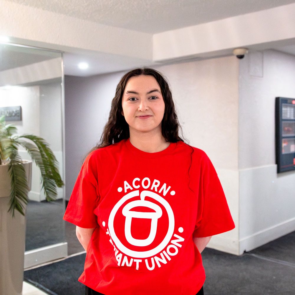 Caitlin poses for a photo while wearing a red ACORN tenant union t-shirt
