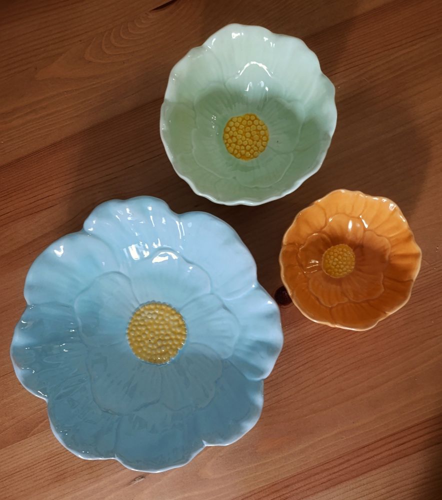 A set of three flower shaped bowls. Bigger one is baby blue, middle one light sage green and smaller one orange. 