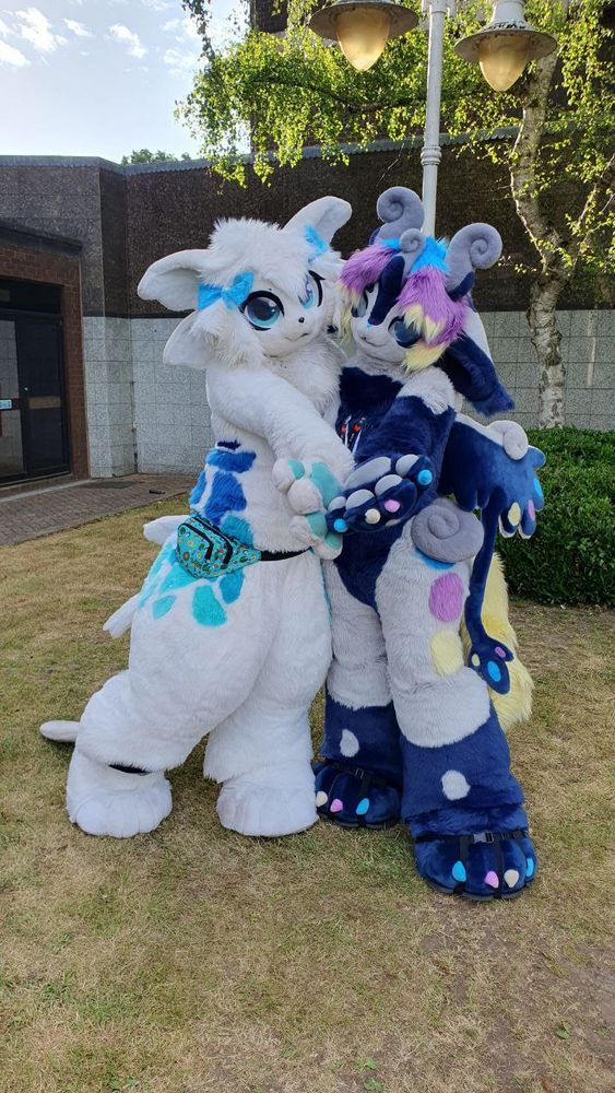 A photograph of Numazu and Parabella standing together, each holding an arm outstretched towards the camera.