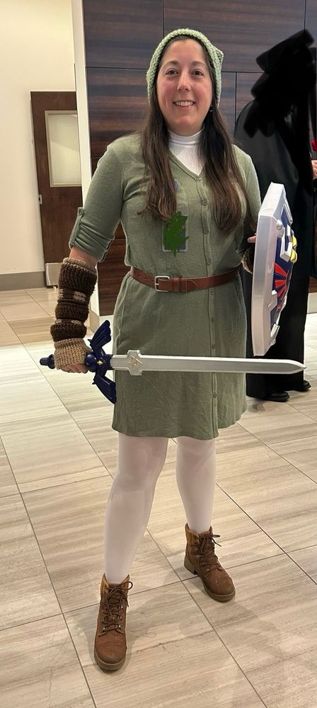Woman with brown hair dressed as Link from the Legend of Zelda series, specifically the OoT/MM era. 