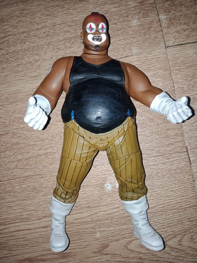 photo of someone's toy. Joker from the movie Akira (1988) dark brown skinned bald overweight man with clown makeup wearing white gloves, tan pants, black tank