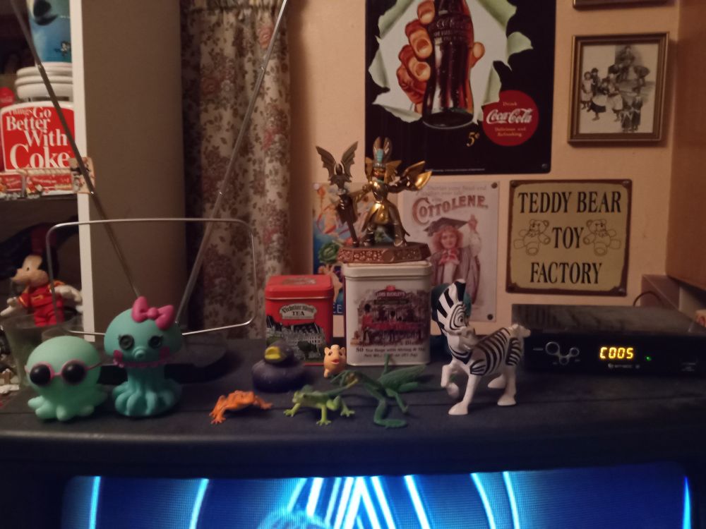 top of the crtv in the kitchen/dining room at my dad's house. Lots of little nik naks. lots of coke products on the shelf to the left, and lots of cool vintage metal posters on the back wall