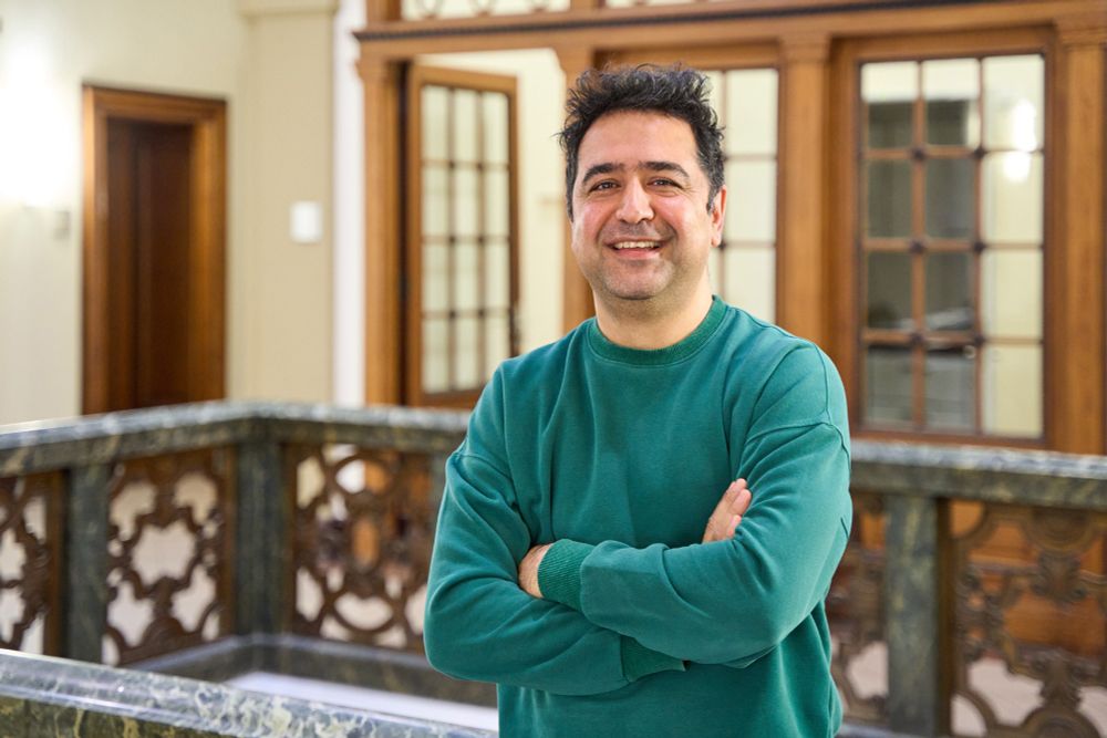Portrait of a man. He is wearing a green sweater. He crosses his arms and laughs.