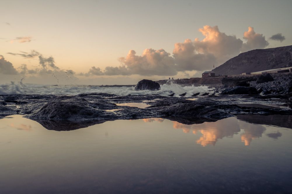 Reflection of rocks and cloud and skyline of beach at dusk
