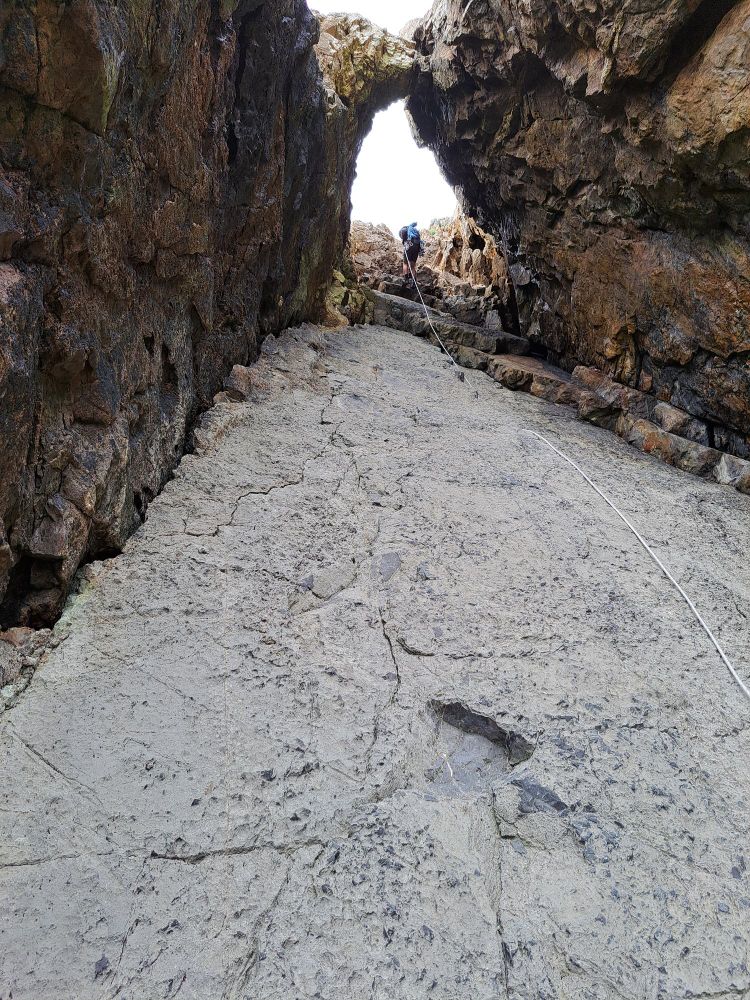 A man abseiling down a slab beneath a rock formation known as Marble Arch