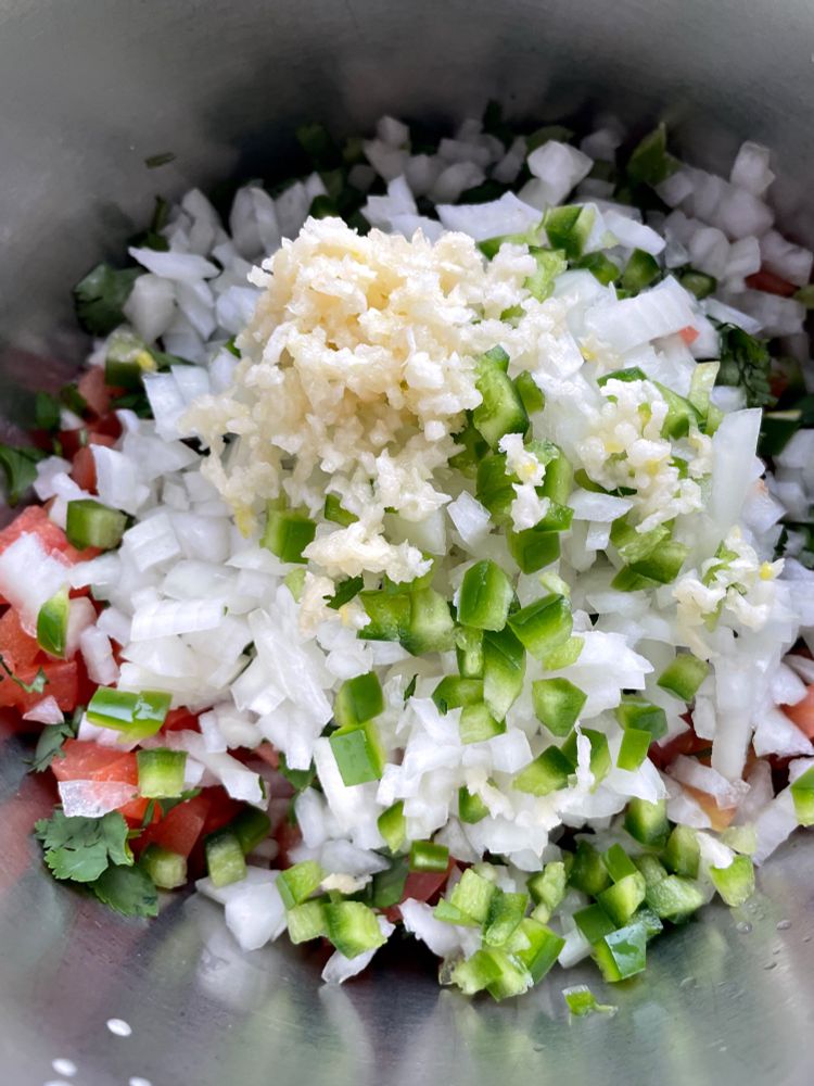 Photo of bowl full of pico de gallo ingredients. Tomatoes, cilantro, onion, jalapeño, and garlic. 