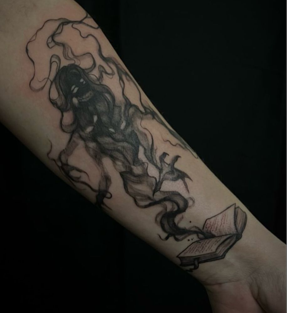 Photo of black ink tattoo on forearm. A multi-clawed shadow creature rising out of a book. 