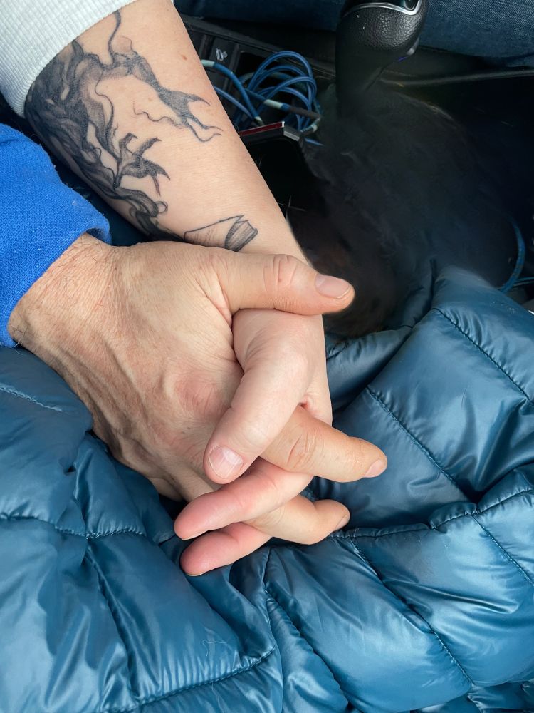 Photo of my hand holding my boyfriend’s hand with a puffy blue coat in background. 