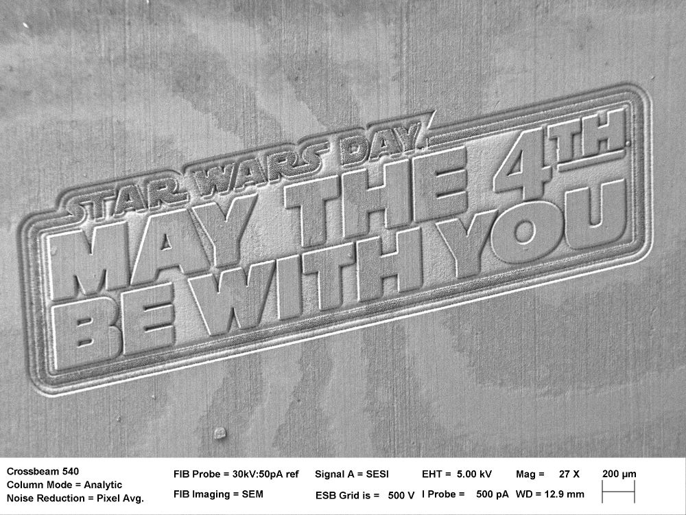 Metal surface engraved with "STAR WARS DAY! MAY THE 4TH BE WITH YOU" viewed under a scanning electron microscope with technical specifications shown below.