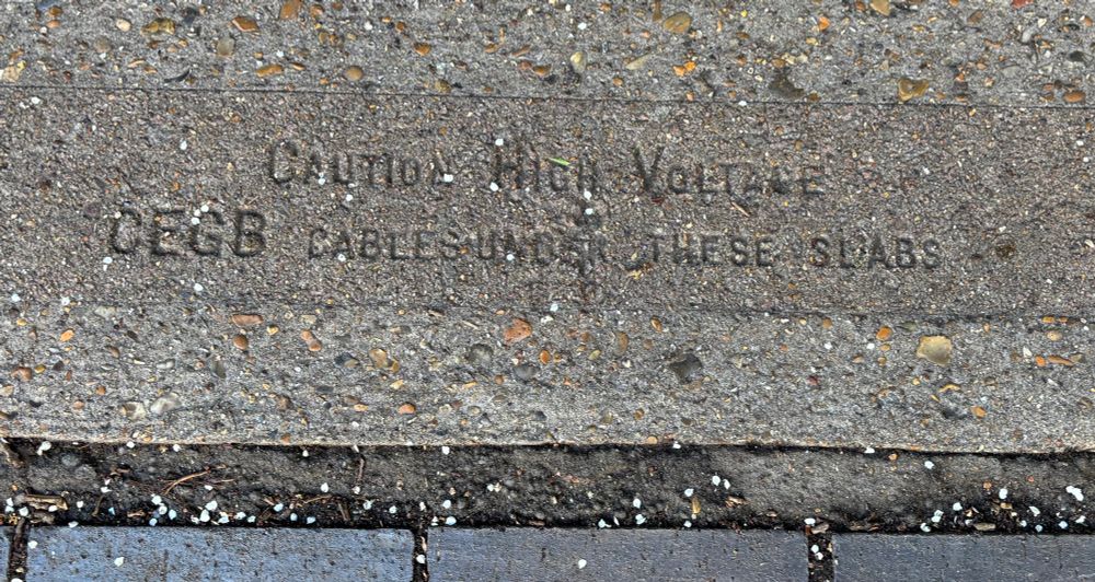 A concrete slab on the canal towpath, with the inscription “Caution High Voltage. CEGB cables under these slabs”.