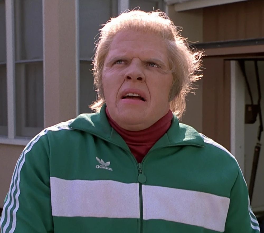 Biff from Back to the Future in a red turtleneck under a green and white Adidas jacket 