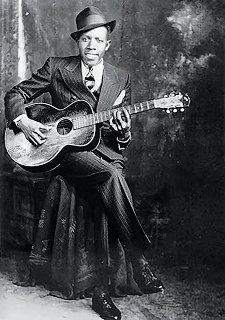 A photograph of Robert Johnson posing with an acoustic guitar 