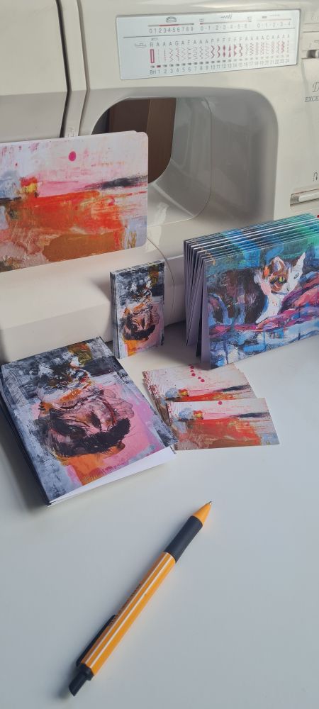Business cards and greeting cards featuring paintings by Julia Laing placed on a white table and leaning against a sewing machine.