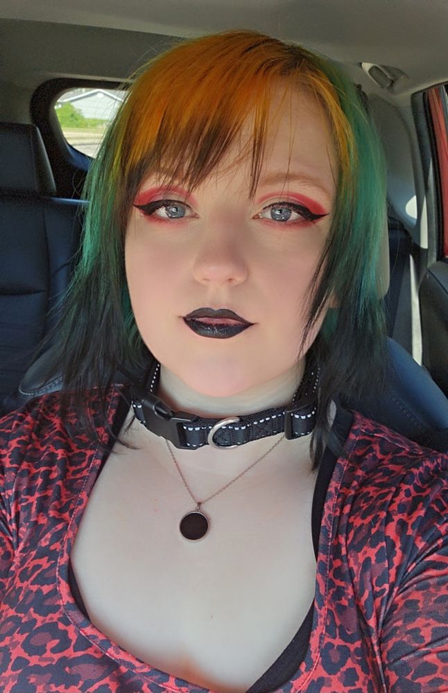 Selfie of me because I did my makeup. My hair is still teal and orange. I did red eyeshadow with black liner and black lipstick. I'm wearing a black collar with a black pendant necklace and red leopard print dress
