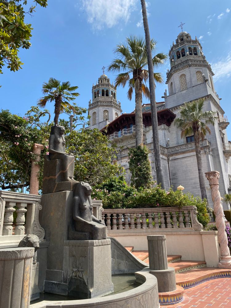 La Casa Grande at Hearst Castle with Egyptian statues in the foreground. Palm trees and foliage stand between the statues and La Casa