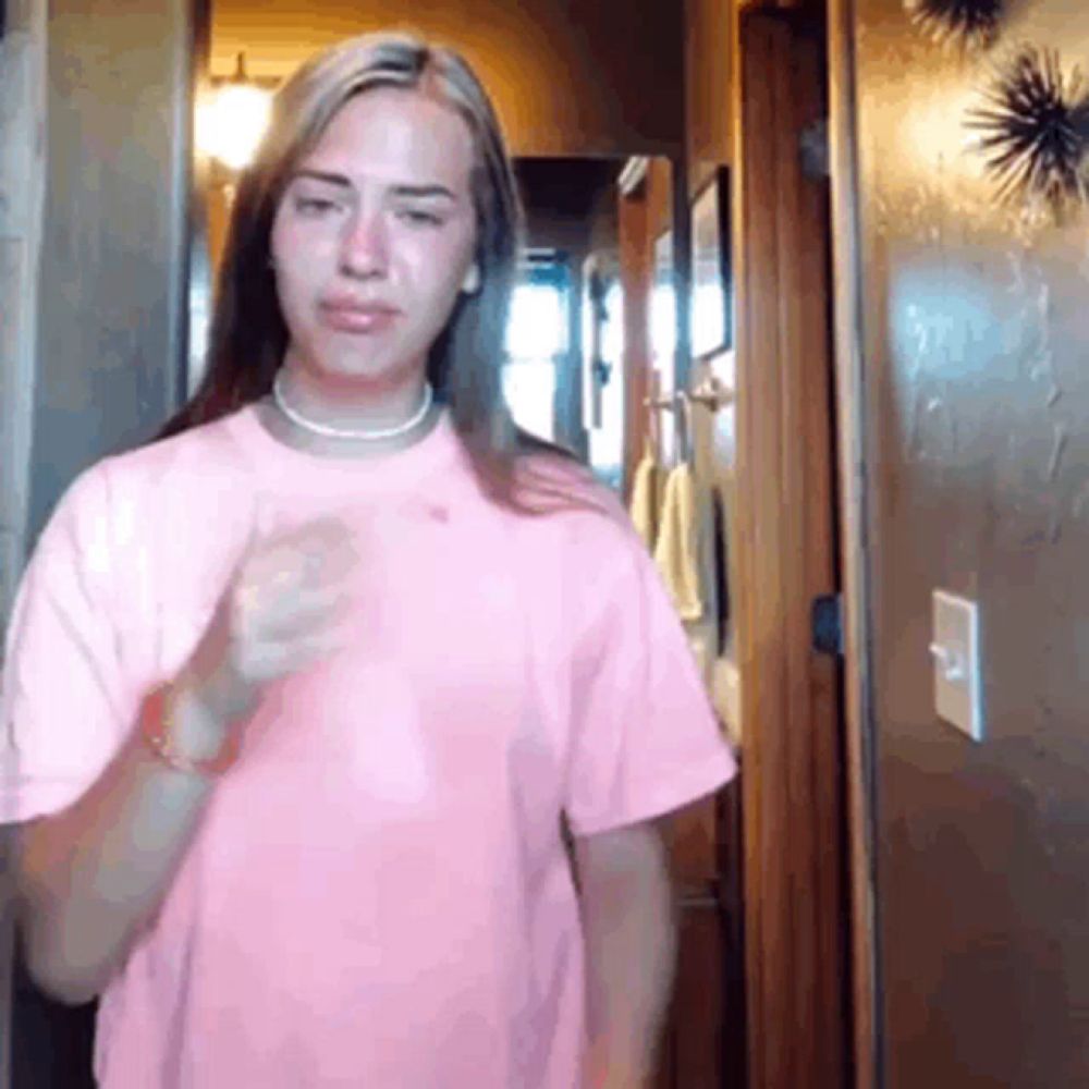 a woman in a pink shirt is standing in a hallway with her hand on her shoulder .