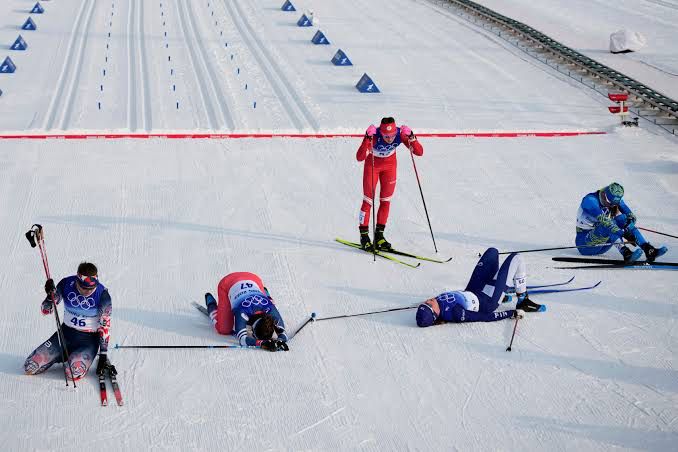 This photos shows five skiers collapsed after crossing the finish line of a skiing race. They are exhausted. 