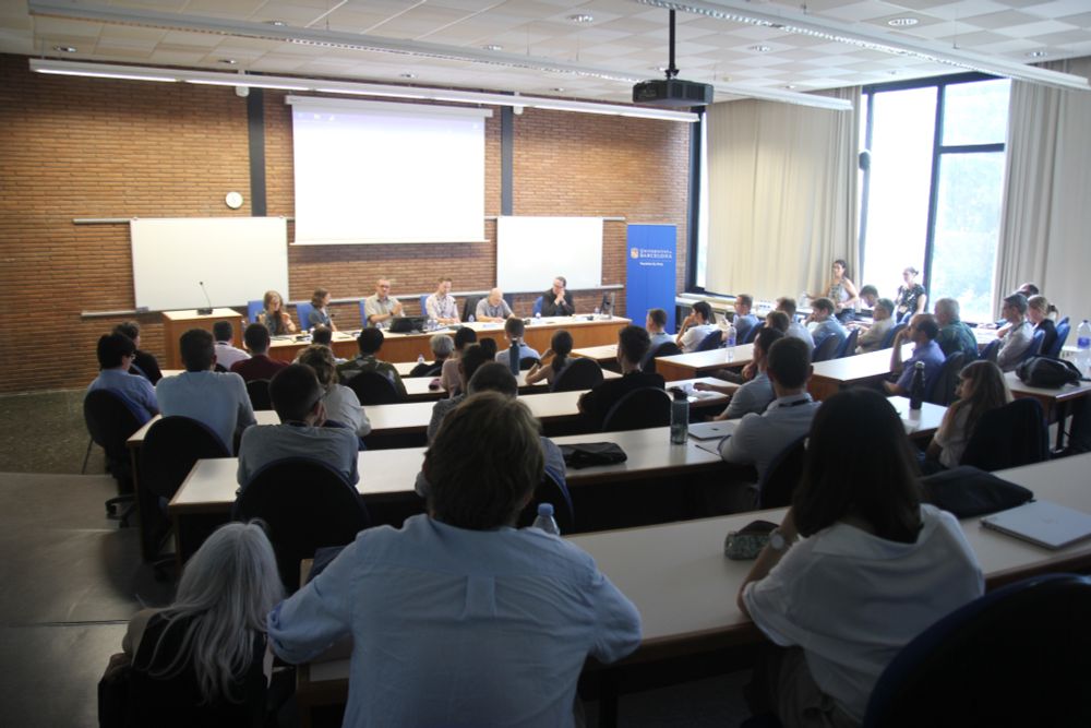 An auditorium with lots of people in the audience listening to a panel at the front of the room talking