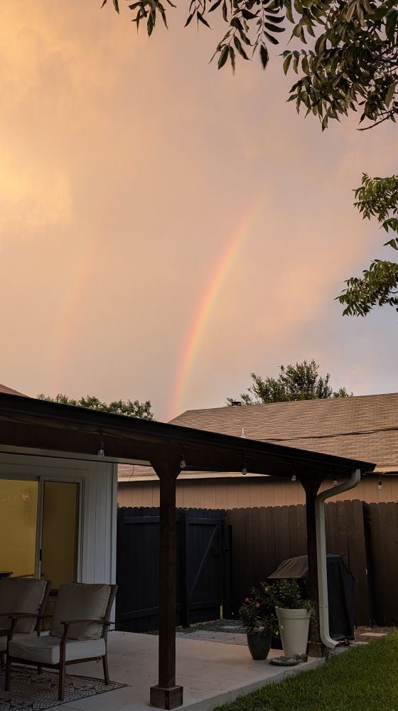 picture of my back patio. Two rainbows are in the sky. One is bright, and the other is more faint. 