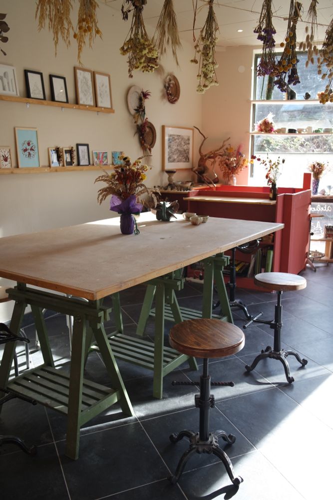 Vue d'atelier avec une grande table, des tabourets et des fleurs séchées 