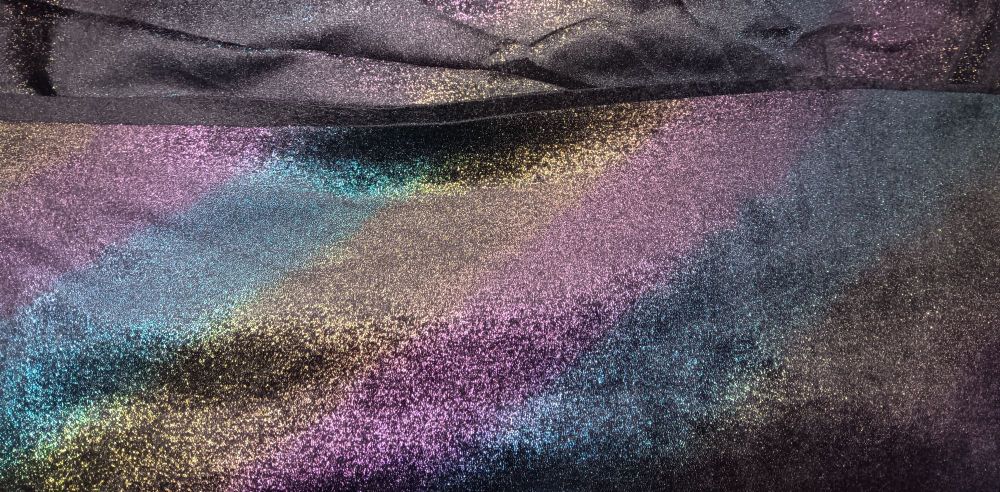 A folded length of black velveteen fabric with a sprayed opalscent rainbow pattern.