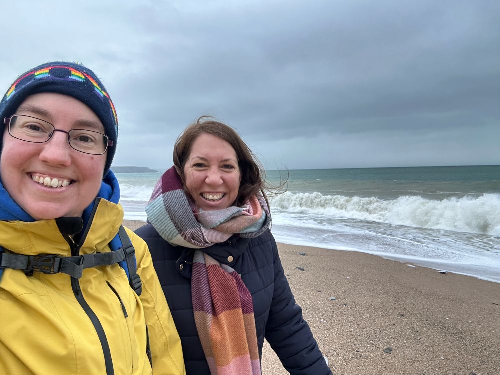 Selfie of Emily and Tabitha on the beach, with waves behind them.