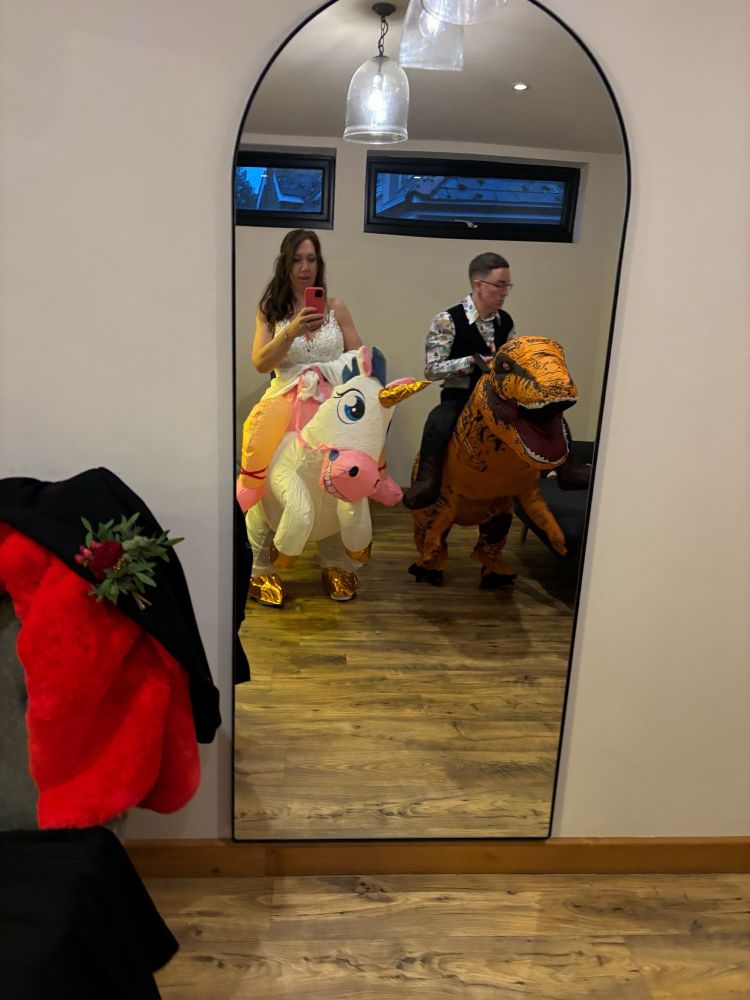 A photo taken in a mirror. In the reflection is Tabitha dressed in an inflatable unicorn and Emily in an inflatable t-Rex.