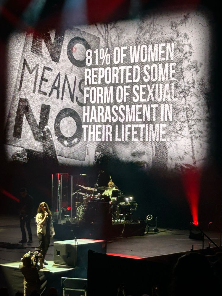 Photo of Alanis Morrisette singing. Behind her is a screen that reads “81% of women reported some form of sexual harassment in their lifetime”.