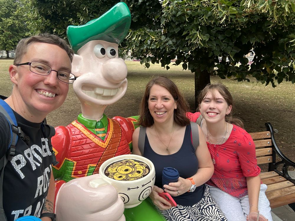 Selfie of Emily, Tabitha and a teenage girl sitting on a bench next to a model of Wallace painted like Robin Hood.