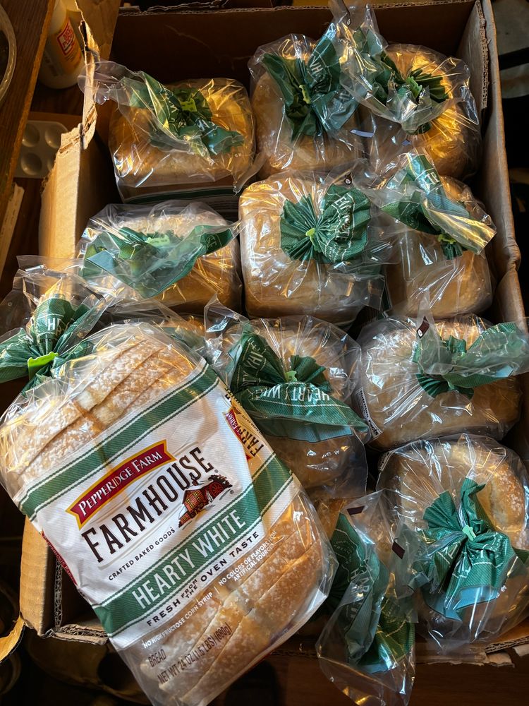 A large box of 12 loaves of bread sitting top up, with one loaf resting on top showing its label of Pepperidge farm farmhouse hearty white bread
