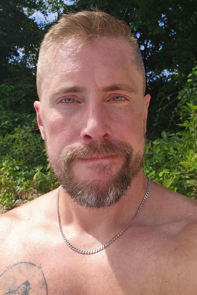 Picture of a shirtless guy with foliage behind him