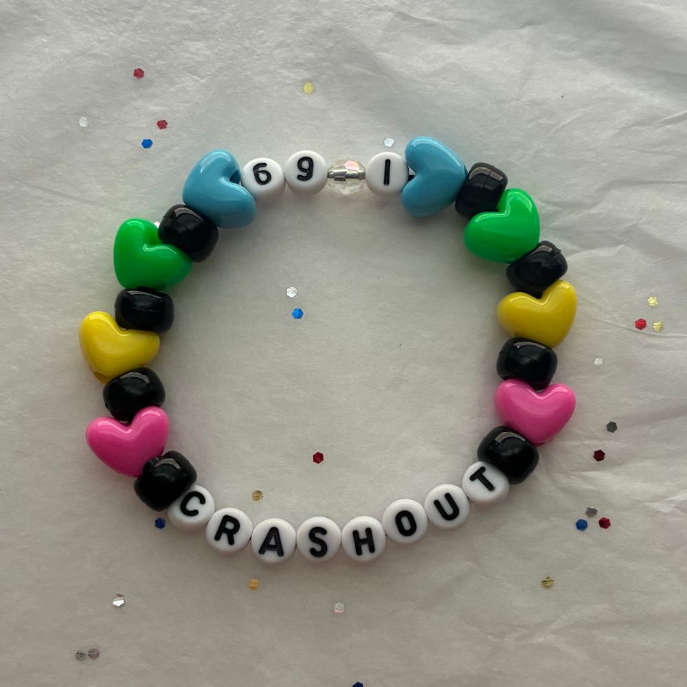 A single beaded kandi bracelet made of black standard round beads, as well as multicolored heart shaped beats in pink, yellow, green, and blue. The letter beads at the front spell out the word crash out. There is number beads in the back as well spelling out I-69 or interstate 69 as a reference to the crash out album cover. 