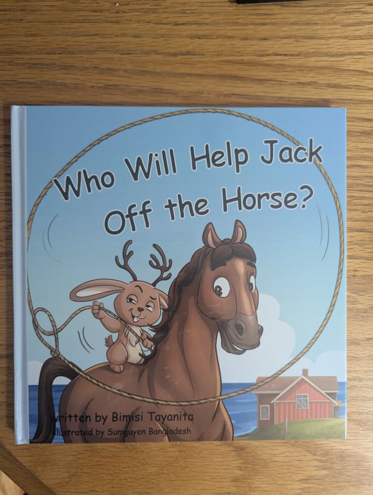 a children's book on a wooden table. the cover has a rabbit twirling a lasso while sitting on the back of a horse. it is entitled 'Who Will Help Jack Off the Horse?'
