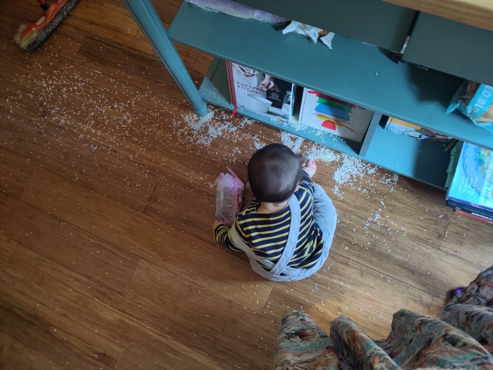 Sur un plancher doré, un bébé assis au milieu de milliers de grains de riz étalés sur le sol