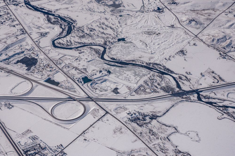 aerial photograph.  Somewhere over Utah, USA.  A wide valley, covered in snow,  with river running down the center.  One road crossing the river. One road running parallel to the river.