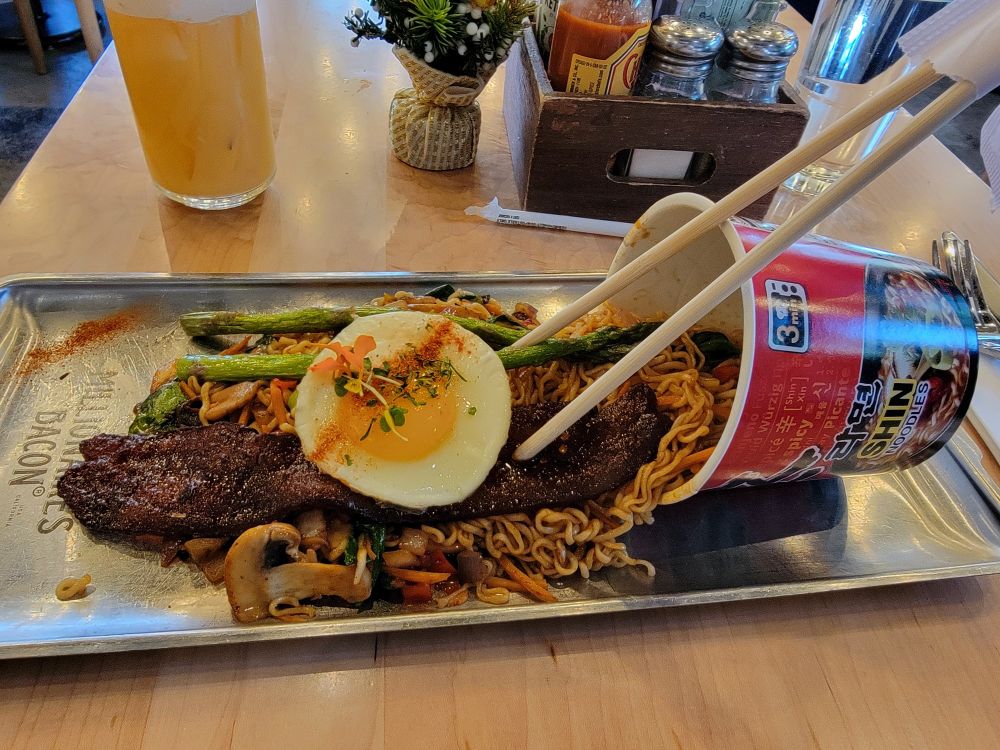 Shin ramen arranged nicely with an egg, a thick slice of bacon, asparagus, and mushrooms.