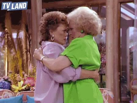 two older women hugging each other in front of a tv land sign .