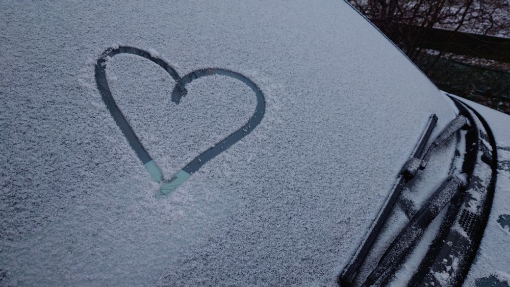 Eine schneebedeckte Frontscheibe eines Autos. In den Schnee wurde ein  Herz gemalt