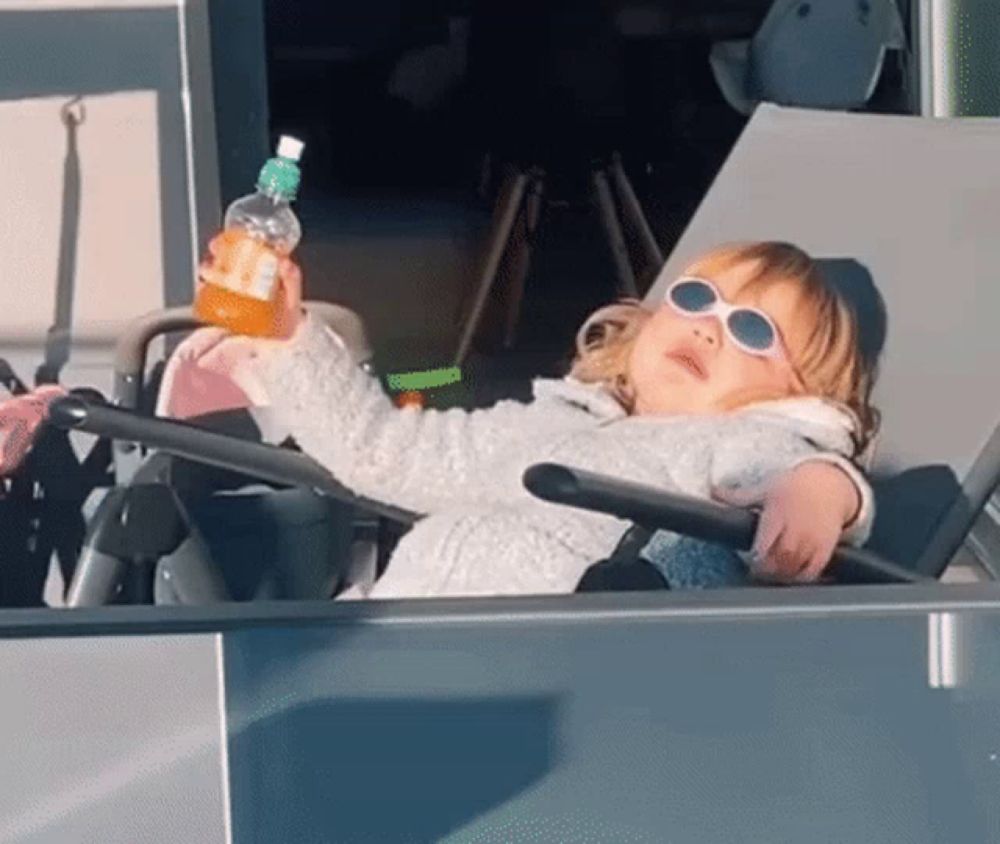 a little girl wearing sunglasses sits in a chair holding a bottle of orange juice