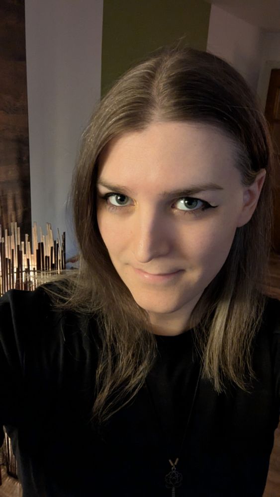 A selfie of myself a trans woman with shoulder length light brown hair and grey eyes, wearing eye make-up. I look at the camera and at this point in time I've been on HRT for 8 months. I also had 9 laser hair removal sessions at this point.