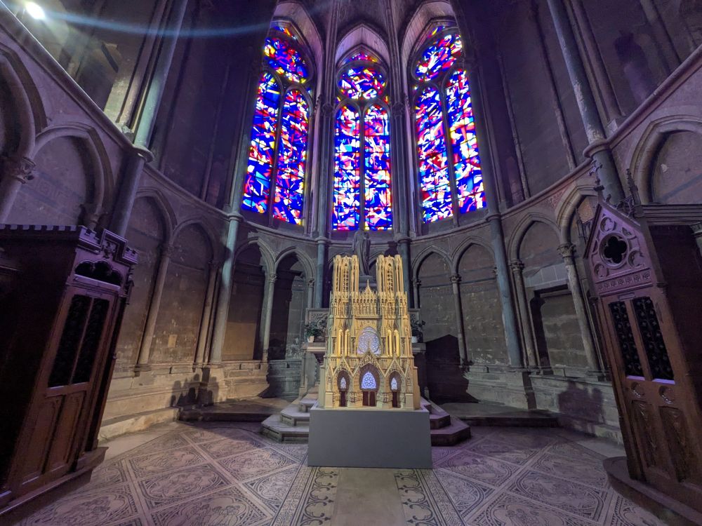 Three tall, long windows with very colorful stained glass windows - a detailed model of the cathedral is the focus of the alcove. Two ornate wood confessionals flank the model. 