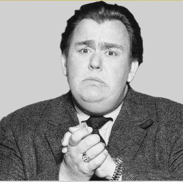 John Candy with a suit jacket, folding his hands with a longing sad face.