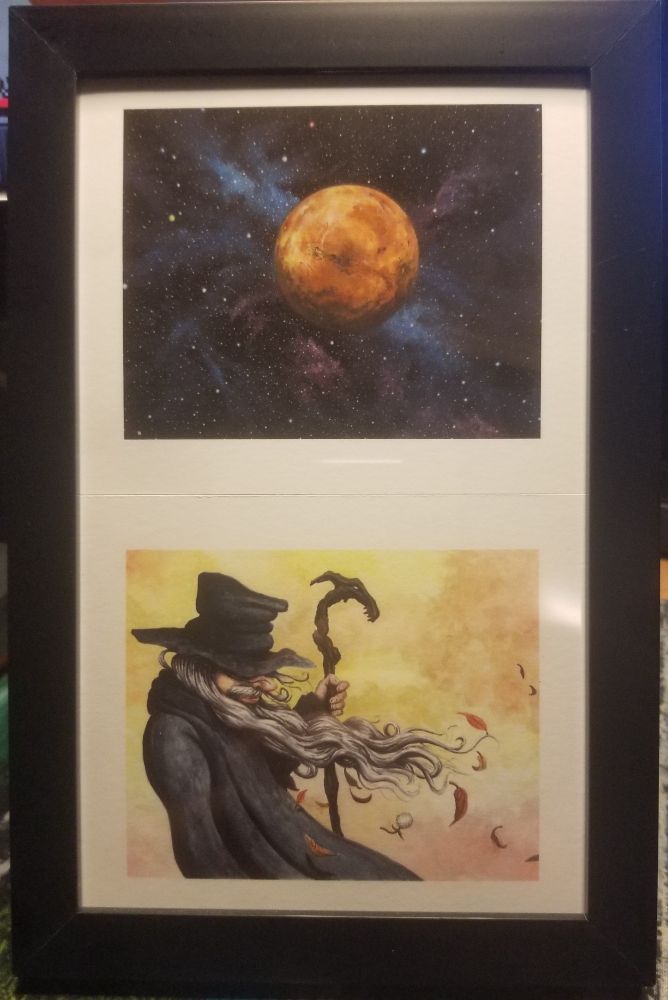 Two prints from MikeZ in a black frame, one of a space scene and one of a wizard in autumn