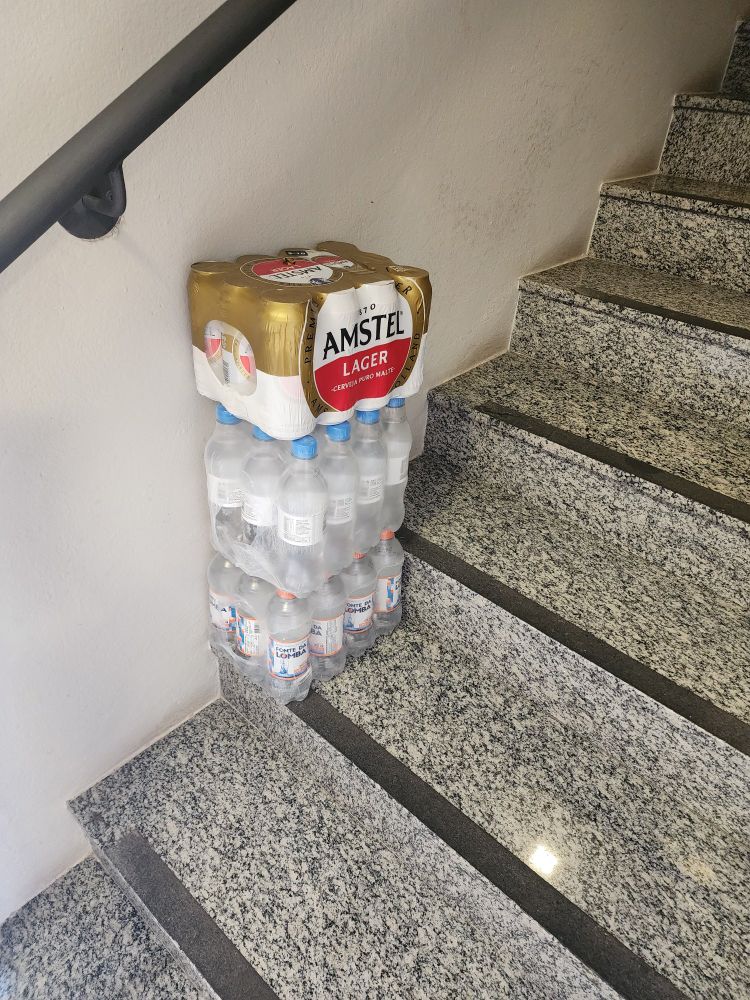 sobre um degrau de escada, dois fardos de água e um de cerveja amstel 
