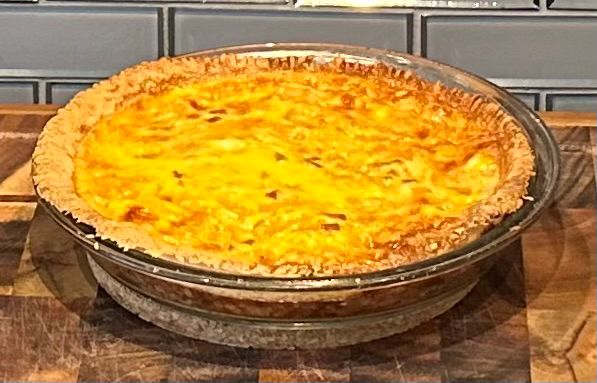 Quiche in a pie pan. Crust has retracted from the edge in most places. 