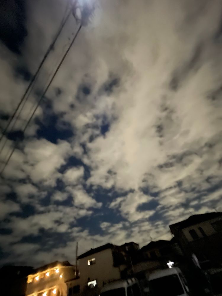 夜の空に白い雲がたくさん浮かんでいます。
下の方に明かりのついた家があります。