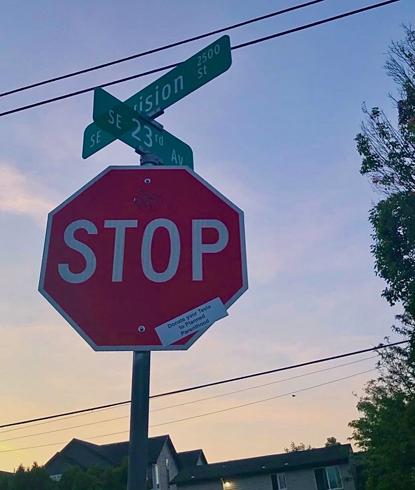 Stop sign at SE Division & 23rd with a slap tag, which reads Donate your Tesla to Planned Parenthood. Lemon-tangerine-peach sunset in the background. 