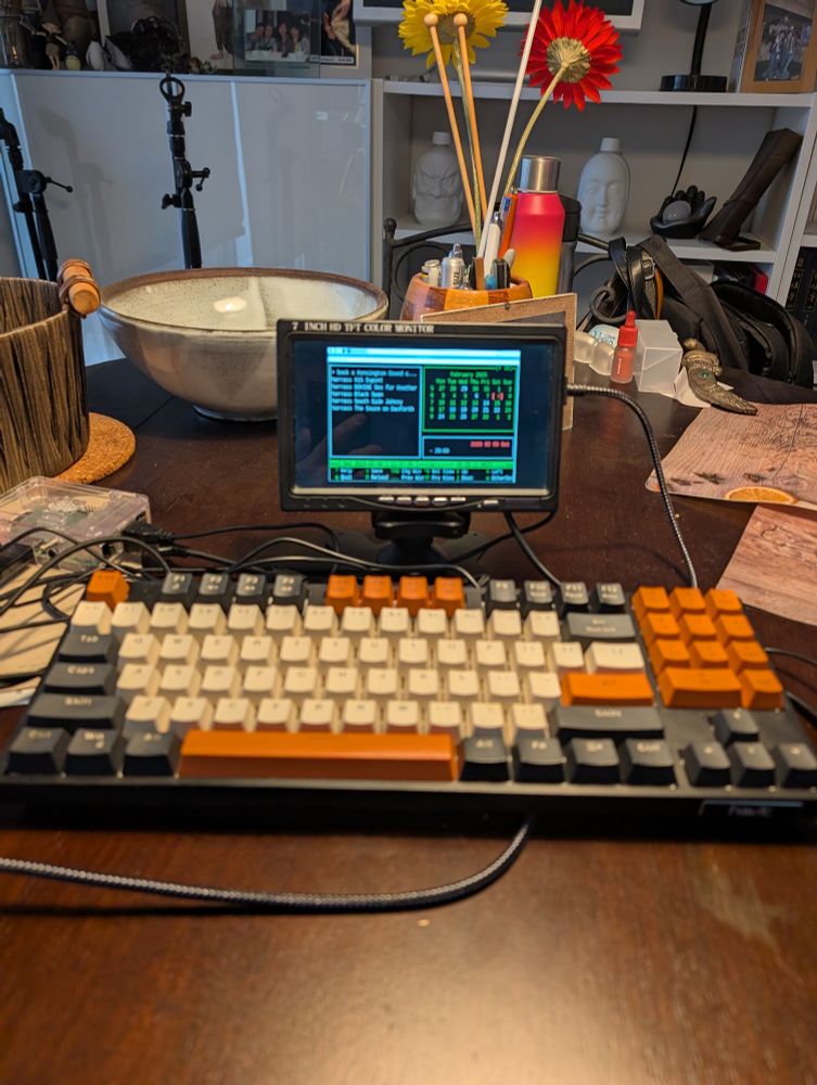 A tiny computer screen and a mechanical keyboard on a busy kitchen table